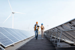 View on the rooftop solar power plant with two engineers walking and examining photovoltaic panels. Concept of alternative energy and its service